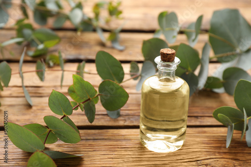 Bottle of eucalyptus essential oil and plant branches on wooden table, space for text