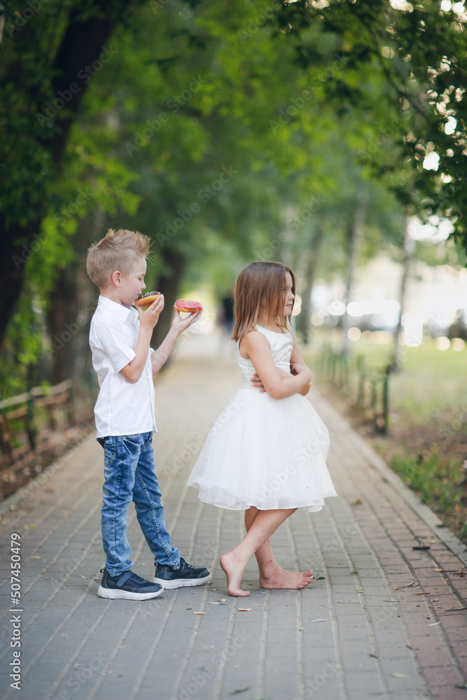 boy child treats harmful offended girl with donuts, asks for forgiveness, wants to make friends. Cute funny romantic couple of kids. boy child treats harmful offended girl with donuts, asks for forgiveness, wants to make friends. Cute funny romantic couple of kids.