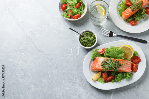 Tasty cooked salmon with pesto sauce and fresh salad on grey table, flat lay. Space for text