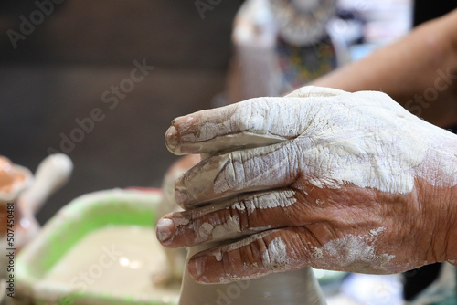 hand of the potter as he shapes a clay pot using light pressure on the material with his sensitive fingers