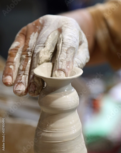 potter while shaping a clay pot on the turning lathe using light pressure on the material with the sensitive fingers photo