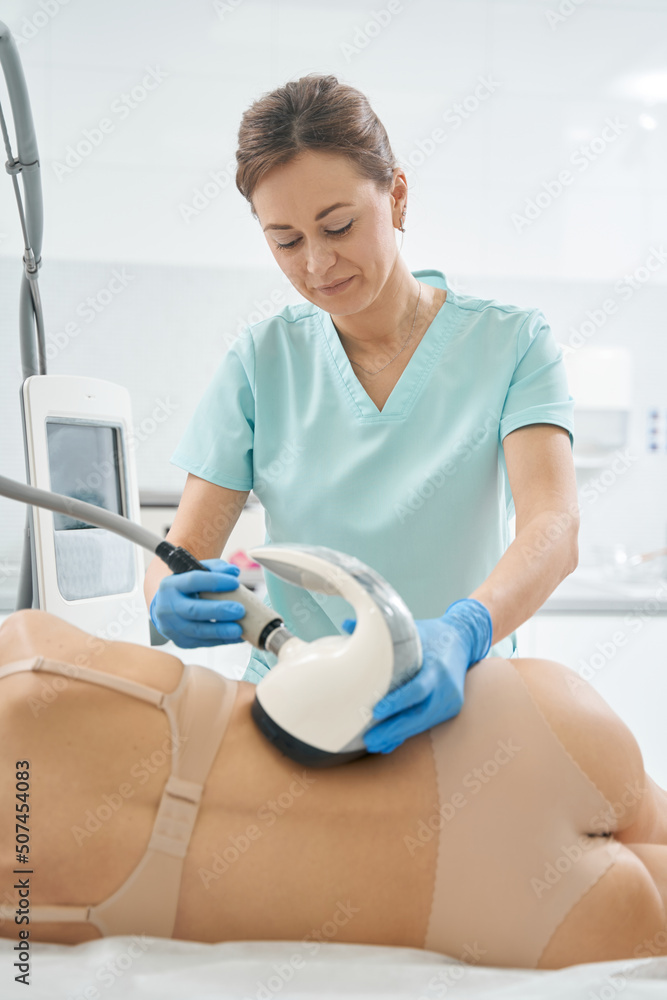 Woman beautician burning fat in patient back with vela shape Woman beautician burning fat in patient back with vela shape