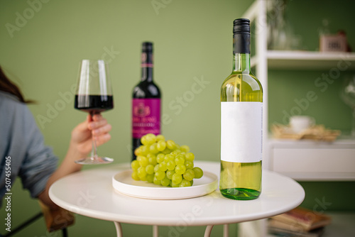 Woman holding glass of red wine over the table with bottles and grapes
