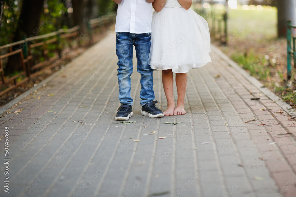 Boy in sneakers and jeans, girl child in white dress and barefoot on the sidewalk in summer Boy in sneakers and jeans, girl child in white dress and barefoot on the sidewalk in summer