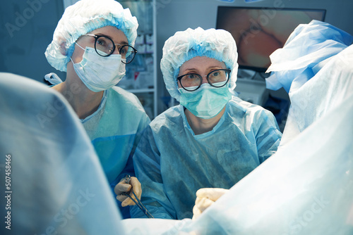 Nurse with surgical scissors and doctor staring at patient pelvis