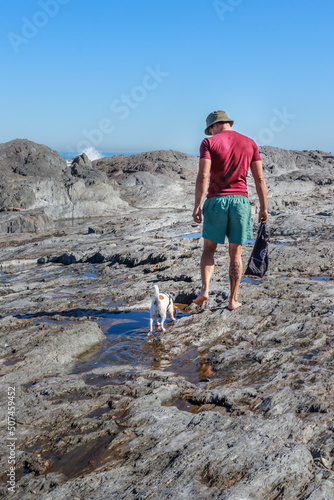 Caucasian Man walking with Jack Russell Terrier dog playing on the beach, Cape Town, South Africa