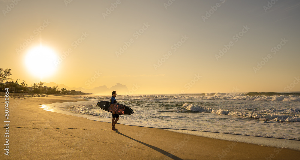 Lindo amanhecer na praia do Recreio, com surfista na areia andando para o mar.