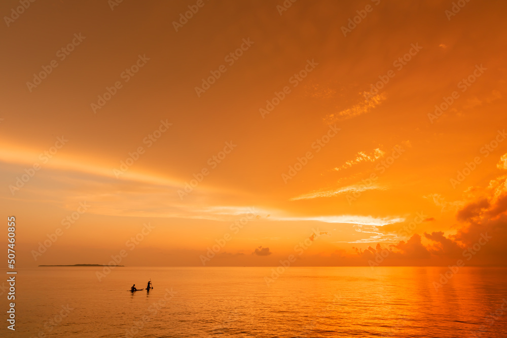 People riding a stand up paddle  on a calm warm sea at an amazing sunrise
