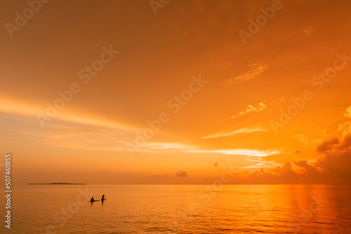 People riding a stand up paddle on a calm warm sea at an amazing sunrise