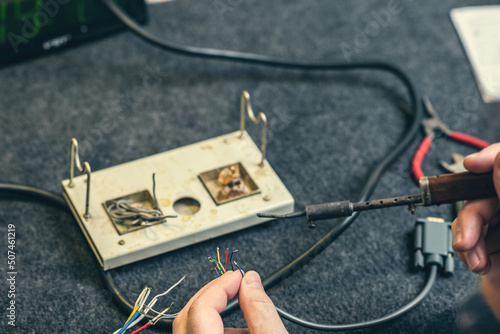 Close - up of male hand with wires and retro soldering iron. Soldering process at home