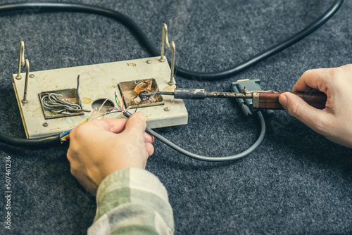 Close - up of female hand and melting wires on the tip of a soldering iron