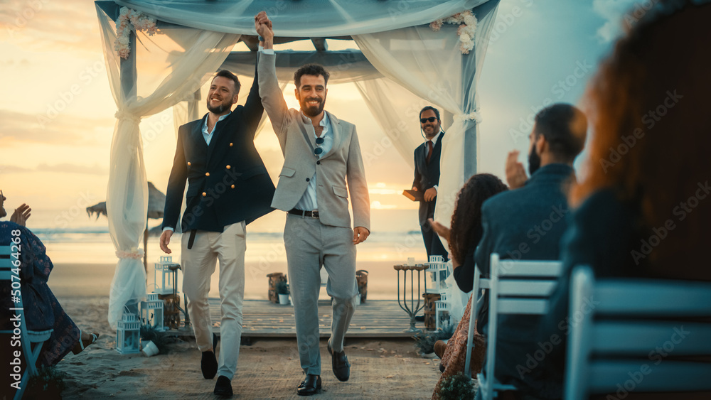 Handsome Gay Couple Exchange Rings and Kiss at a Beach Wedding Ceremony Venue at Sunset. Two Happy Men in Love Share Their Big Day with Diverse Multiethnic Friends. LGBTQ Relationship Goals. - obrazy, fototapety, plakaty 