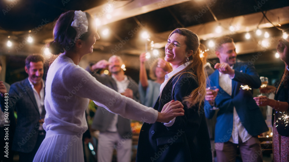 Beautiful Happy Lesbian Couple Celebrate Wedding at an Evening Reception Party with Diverse Multiethnic Friends. Queer Newlyweds Dancing and Kissing at a Restaurant Venue. LGBTQ Relationship Goals.