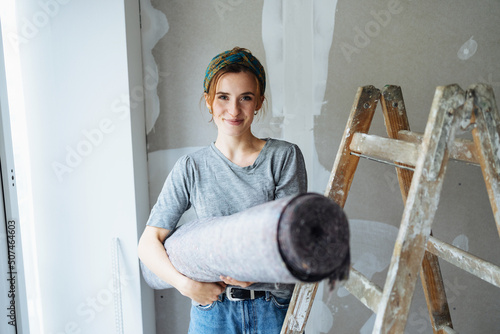 Young woman renovating her bedroom and has a painter carpet in her hand photo