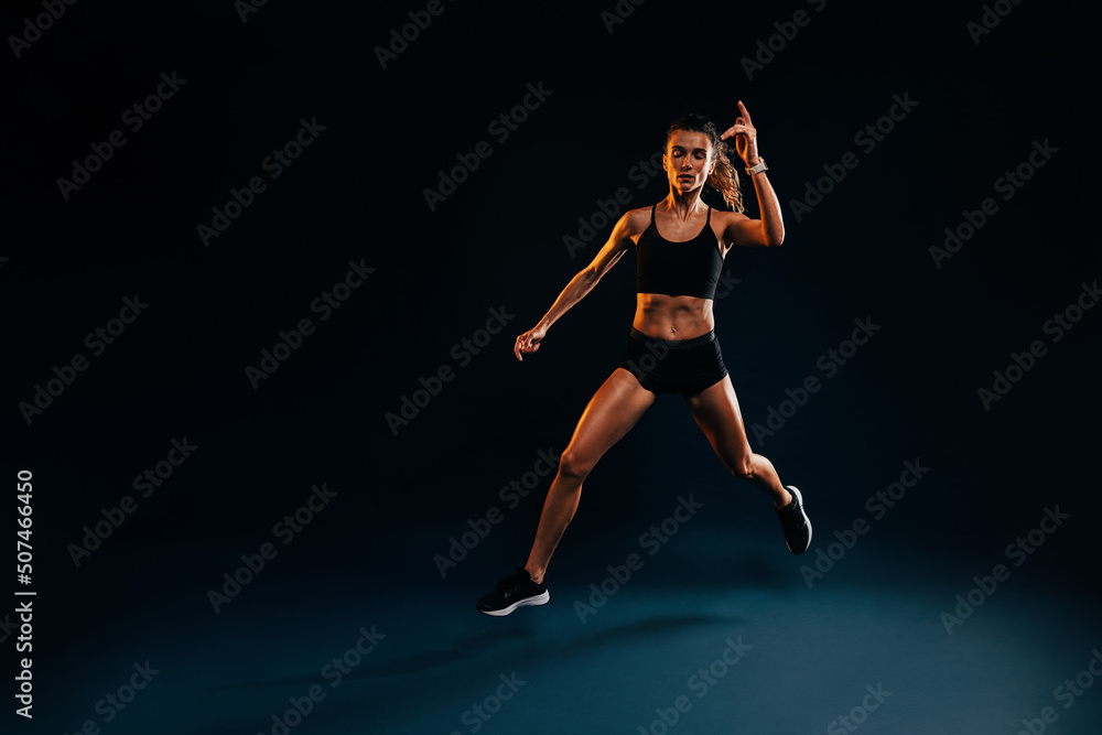 Young woman runner jumping in studio. Muscular athlete exercising on black backdrop. Young woman runner jumping in studio. Muscular athlete exercising on black backdrop.