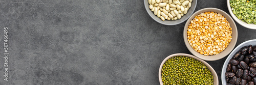Banner of different types of legumes in bowls, yellow and green peas and lentils, colored beans and maash, top view, copy space