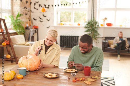 Billede på lærred Positive young multi-ethnic friends sitting at wooden table and enjoying Hallowe
