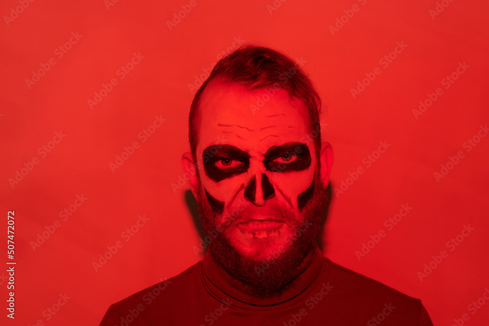Portrait of angry bearded zombie man with gloomy makeup standing in red light, Halloween concept Portrait of angry bearded zombie man with gloomy makeup standing in red light, Halloween concept