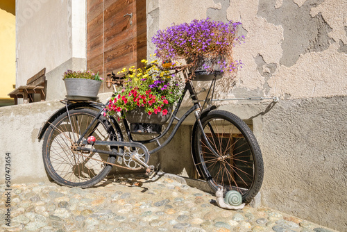 An old rusty bike, decorated with beautiful flowers, in the historic village center of S-Chanf (Upper Engadine Valley , Grisons, Switzerland). It probably hasn't been ridden in a long time. photo