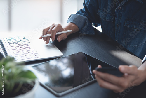 Close up of casual business man working on laptop computer, using mobile phone and digital tablet on office table