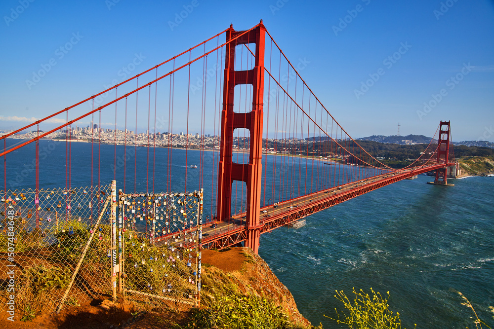Fototapeta premium Fence covered in locks next to Golden Gate Bridge at Sunset