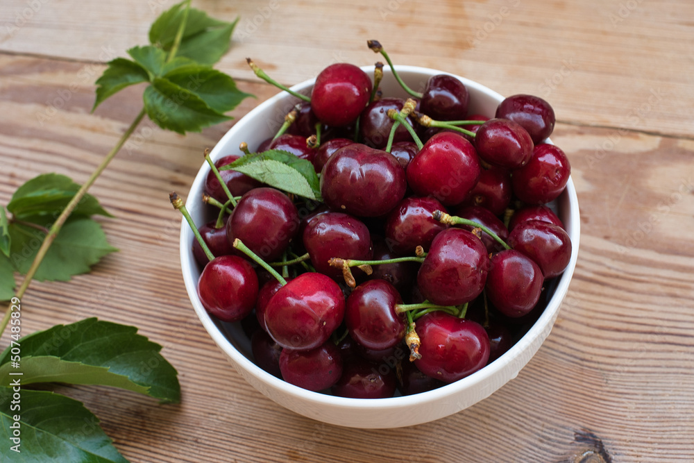 Ripe red cherries in a bowl and next to it on wooden table Ripe red cherries in a bowl and next to it on wooden table