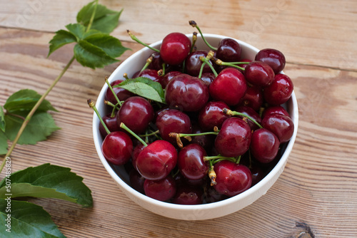 Ripe red cherries in a bowl and next to it on wooden table