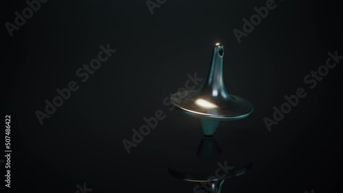 The closeup of a spinning top spins and moves towards the camera, then slows down, swings and stops. The spinning top spins on the black surface.