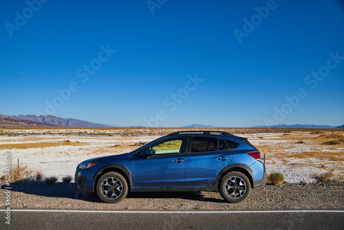 Fototapeta Naklejka Na Ścianę i Meble -  Blue Subaru Crosstrek parked on road with white sand desert in background outside Death Valley