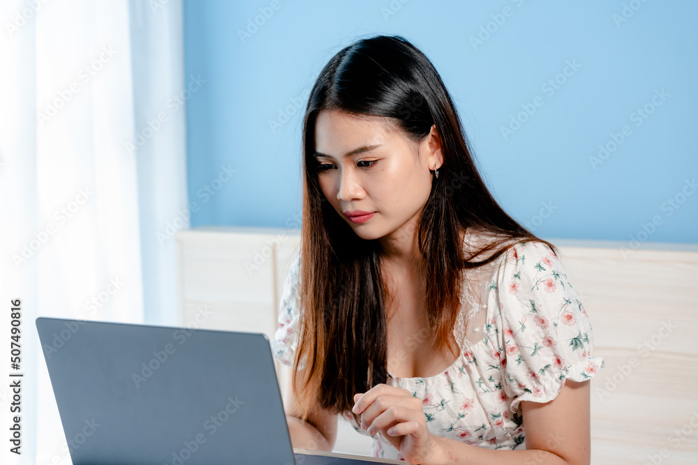 Beautiful Asian girl, wearing a floral shirt, is ordering online on a laptop computer, happily, holding a credit card in her hand, picking up to pay with a credit card,online shopping. Beautiful Asian girl, wearing a floral shirt, is ordering online on a laptop computer, happily, holding a credit card in her hand, picking up to pay with a credit card,online shopping.