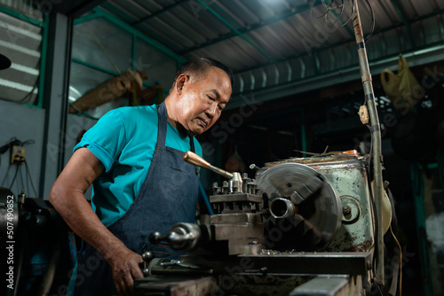 Portrait of Asian senior man working as a steel lathe is preparing work and equipment to turn steel and a small lathe in the family industry.