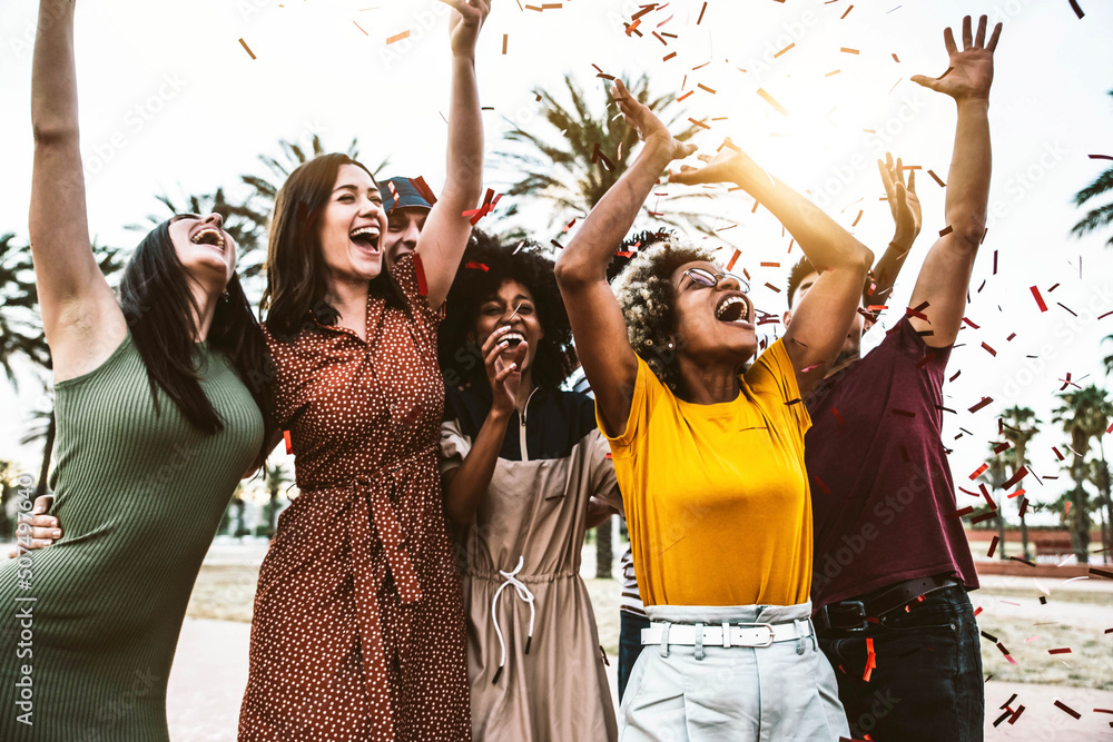 Group of young people throwing confetti in the air making festival party Multiracial friends