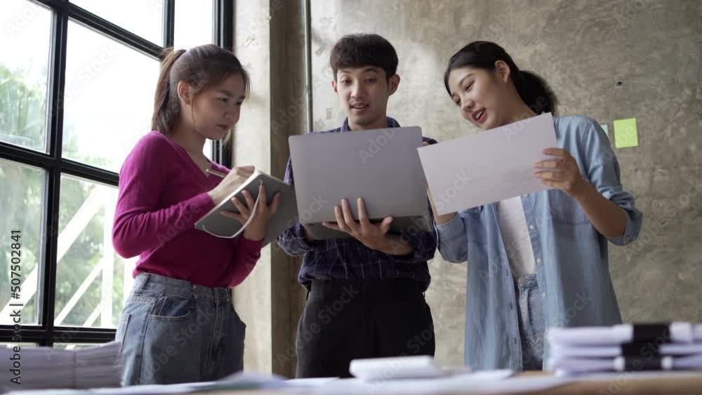 Group of young Asian business people stand work together in office. Concept of presentation new idea business project. Group of young Asian business people stand work together in office. Concept of presentation new idea business project.
