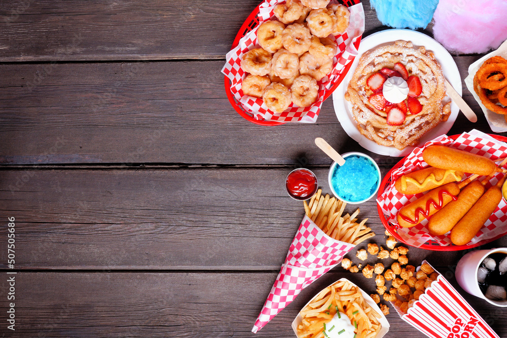 Carnival theme food side border over a dark wood background. Top view with copy space. Summer fair concept. Corn dogs, funnel cake, cotton candy and snacks. - obrazy, fototapety, plakaty 