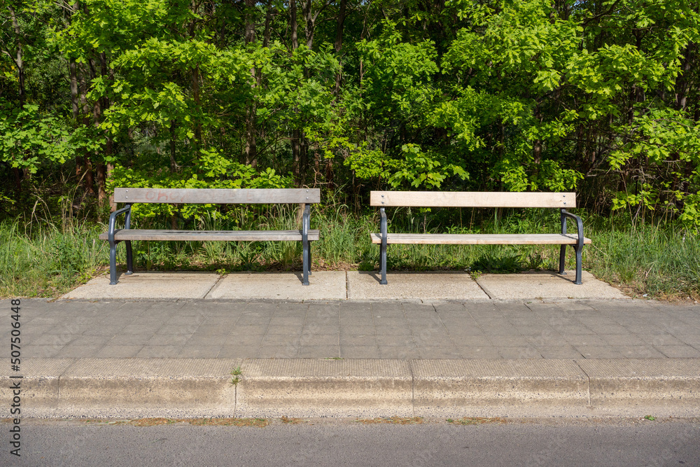 Two empty roadside benches in front of green bushes implying a solitude Two empty roadside benches in front of green bushes implying a solitude