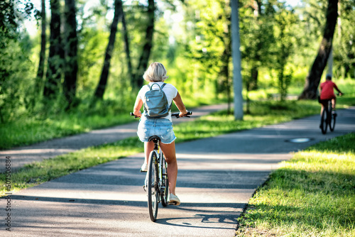 A young woman riding a bicycle in a park in summer.