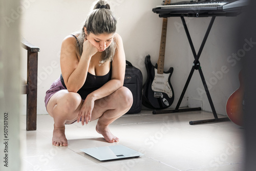 Obraz na plátně beautiful latina woman very bored looking at her weight on the scale after weighing herself
