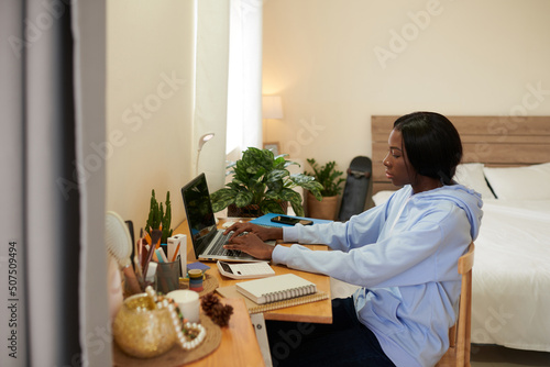Smart female college student working on laptop in her bedroom, preparing for online test photo