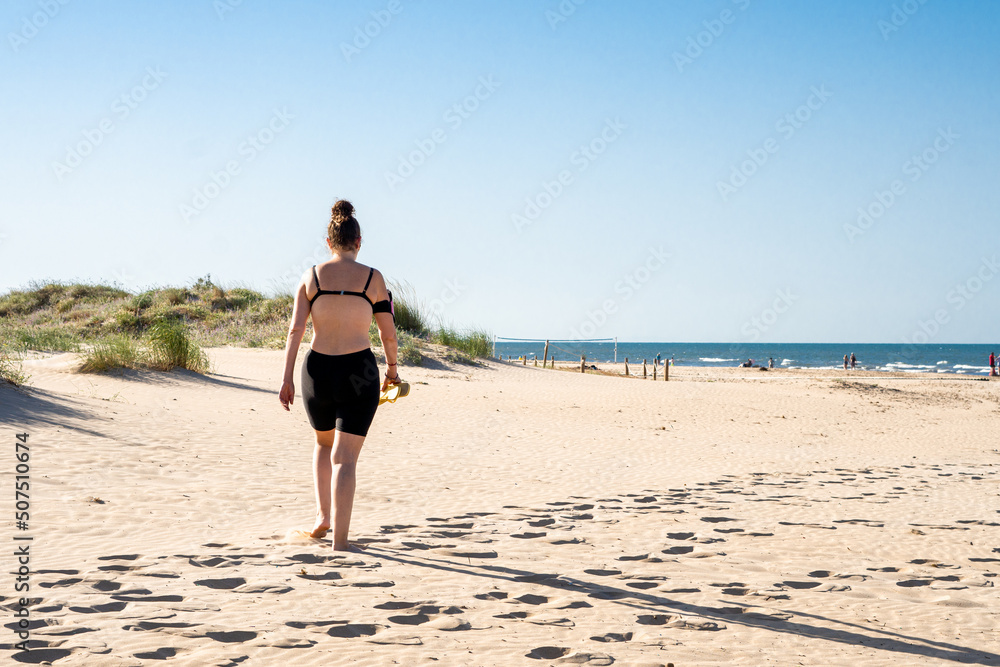 Rear view of a woman walking on the fine sand of the beach at sunset.