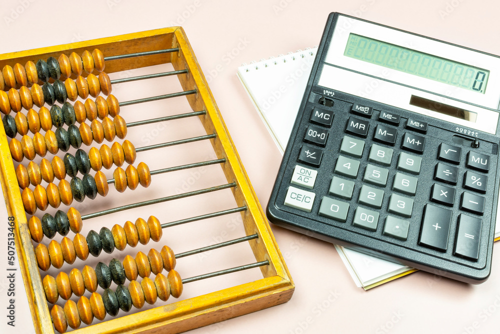 Old antique wooden abacus and a modern calculator lying on a notepad on a pink background close-up. Transition to modern technologies. Progress in accounting, business, finance. Old antique wooden abacus and a modern calculator lying on a notepad on a pink background close-up. Transition to modern technologies. Progress in accounting, business, finance.
