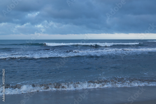 Lone surfer riding a wave under a stormy sky with tanker ship on distant horizon 