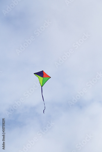 Multi coloured kite with tail ribbon flying against a cloudy sky © Mark