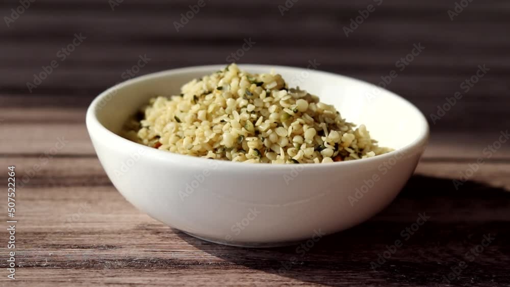 Organic cannabis seeds are poured into a small white plate with a spoon on a wooden background. Organic cannabis seeds are poured into a small white plate with a spoon on a wooden background.