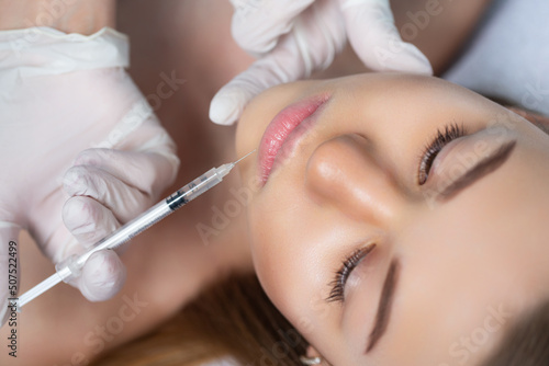 Attractive young woman is getting a rejuvenating facial injections. She is sitting calmly at clinic. The expert beautician is filling female wrinkles by hyaluronic acid