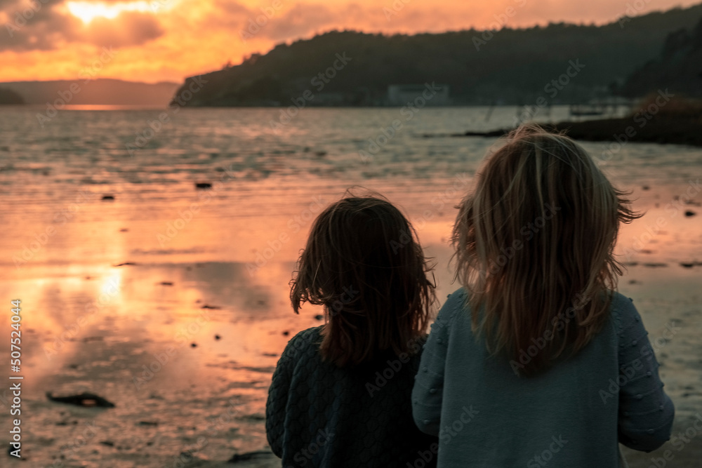 two little girls are watching a beautiful sunset on the seashore