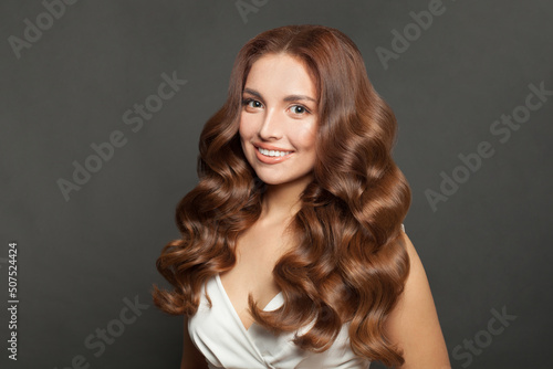 Lovely woman with curly beautiful hair smiling on gray background.