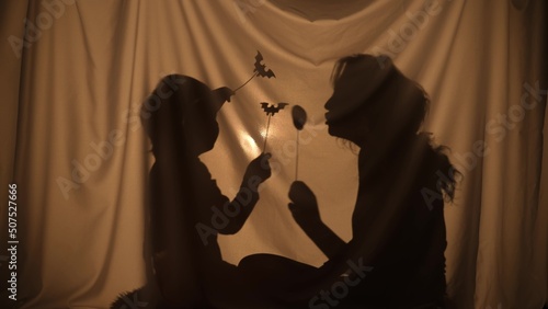 Unrecognizable woman and boy telling spooky stories using shadow play and paper bats and pumpkins. Mom and son have fun, sitting behind the curtain at home. Puppet theater of shadows. Close up.