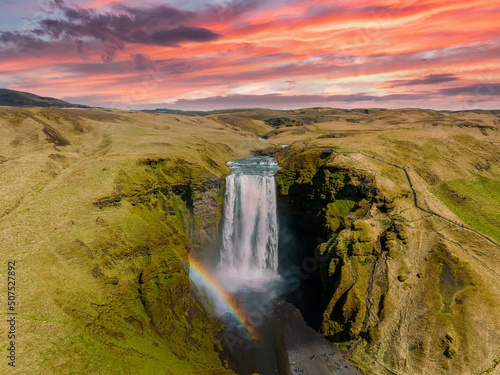 Famous Skogafoss waterfall with a rainbow. Dramatic Scenery of Iceland during sunset. Majestic Skogafoss Waterfall in countryside with colorful sky aerial scenic view.