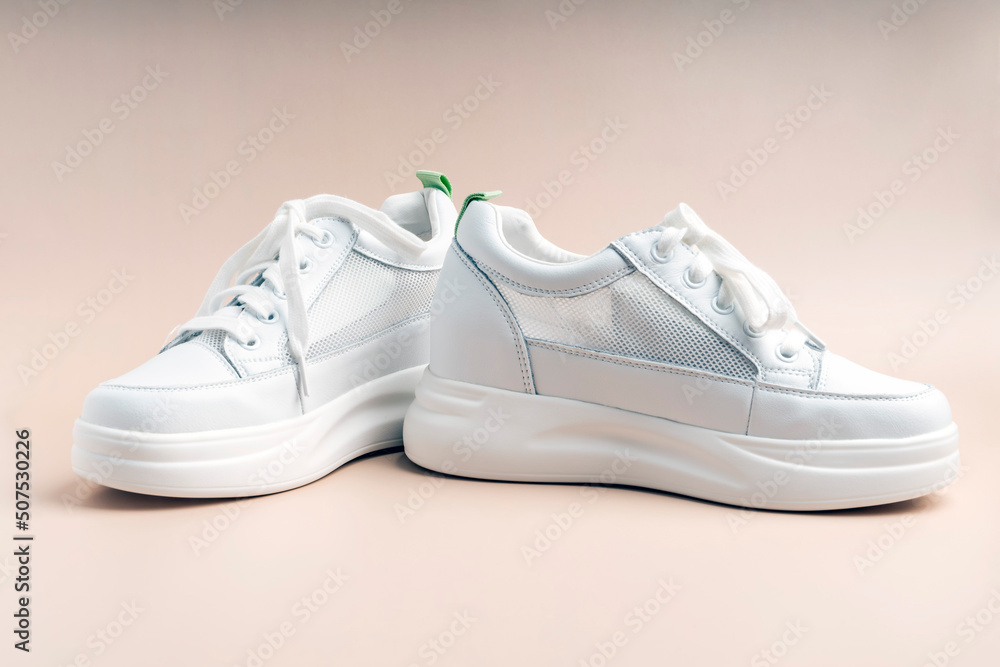 White sneakers with a net on the sides on a beige background