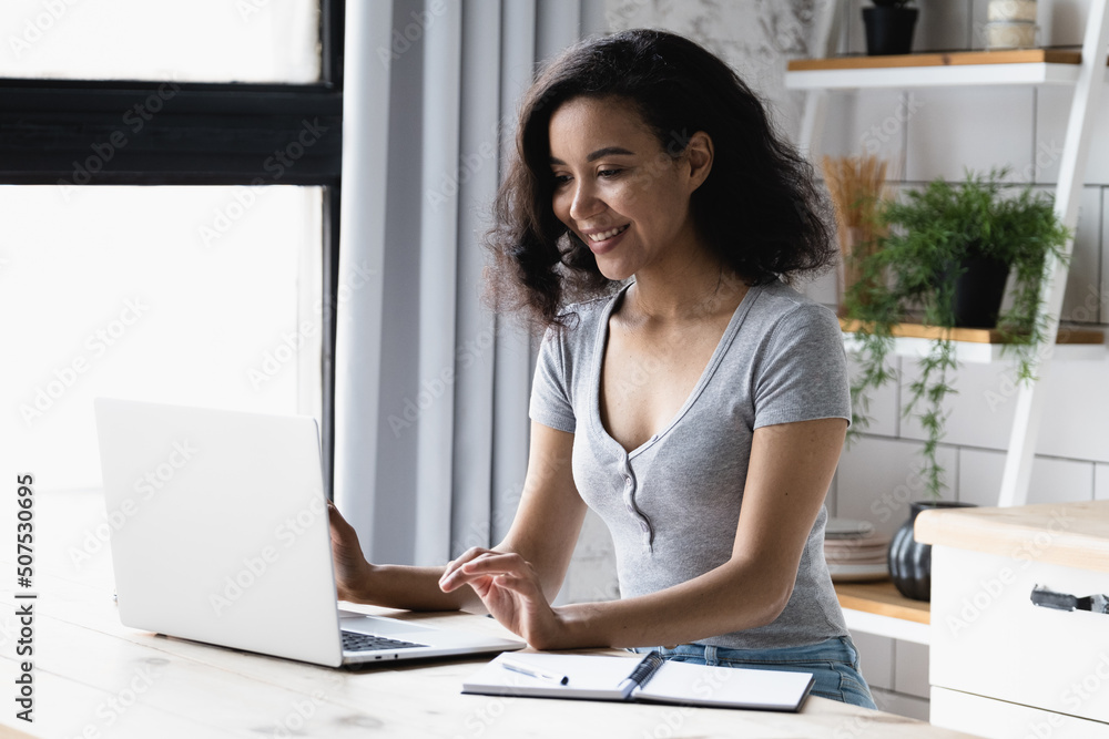 Happy African American woman using computer, looking at device screen smiling reading message browse social networks, interacting online, blogger chatting in internet, distance learning education Happy African American woman using computer, looking at device screen smiling reading message browse social networks, interacting online, blogger chatting in internet, distance learning education